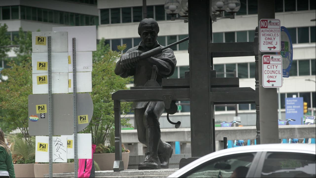 Estatua de Benjamin Franklin manejando una imprenta en el centro de la ciudad.